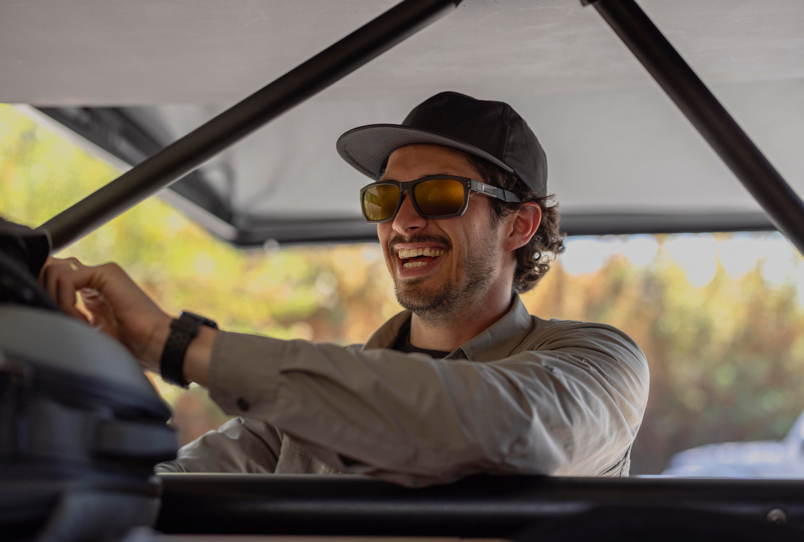 Man wearing sunglasses and a cap inside a vehicle with a blurred natural background