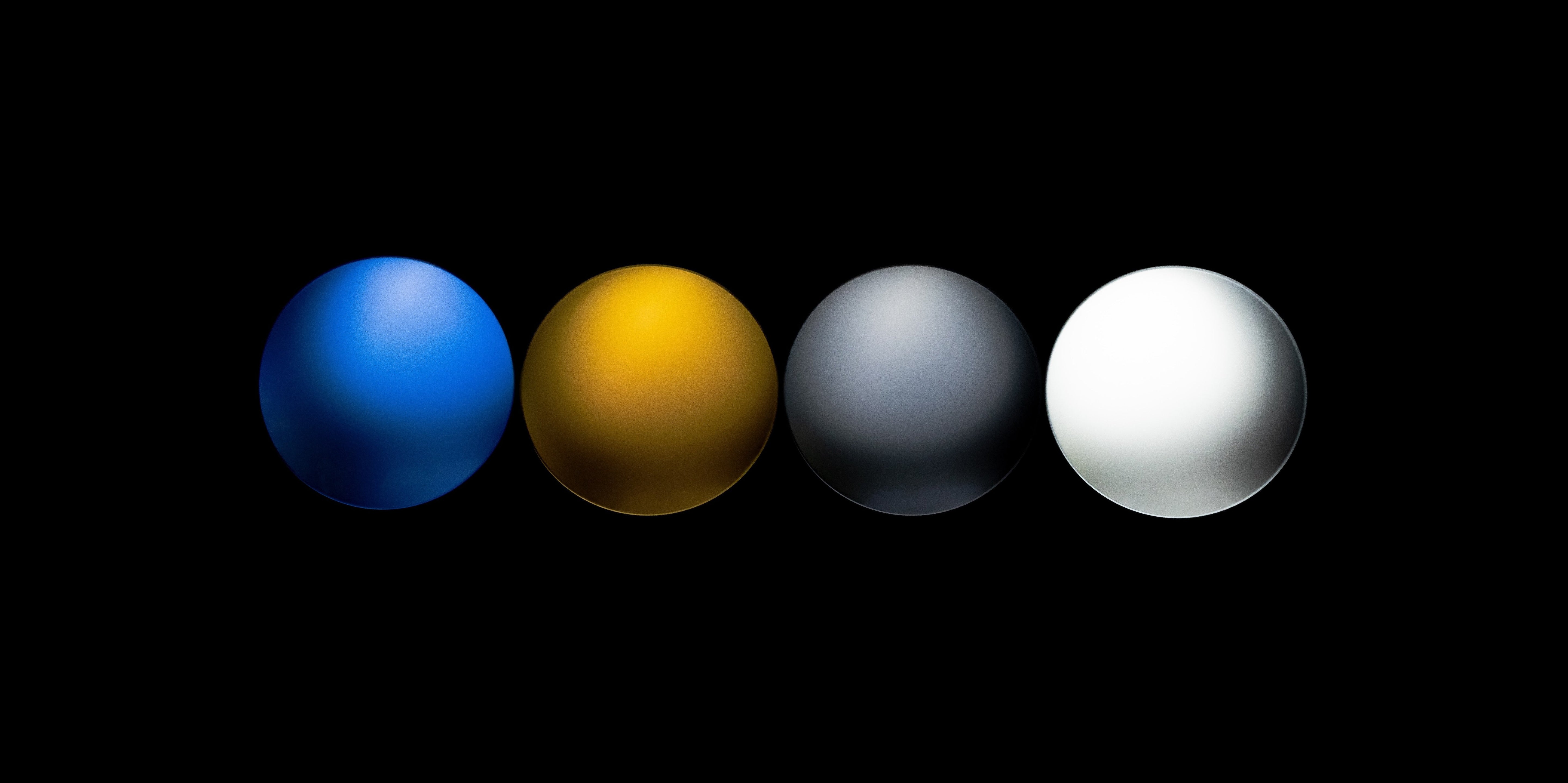 Four spherical objects in blue, yellow, gray, and white on a black background