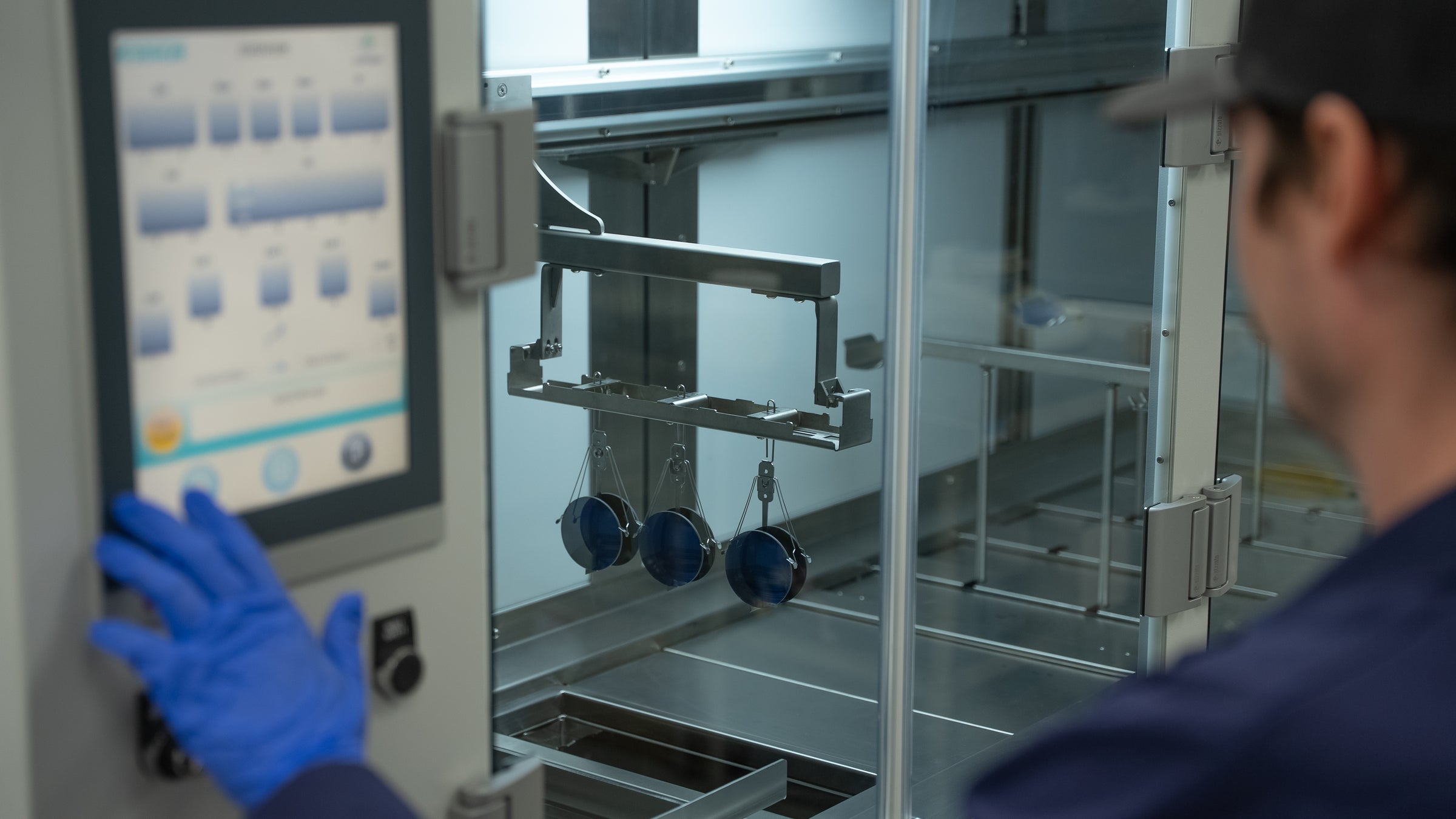 Person in a laboratory setting interacting with a machine using a touch screen.